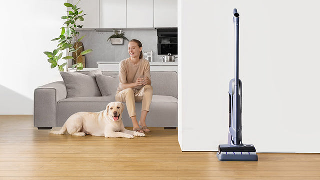 Narwal S20 Pro cordless vacuum mop standing next to a relaxed person and their dog in a cozy living room.